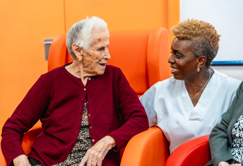 two women engaging in friendly conversation in a colorful care setting elderly care support with 8 happy moments