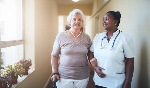 smiling elderly woman walking with nurse in hallway wellness seven care elderly support