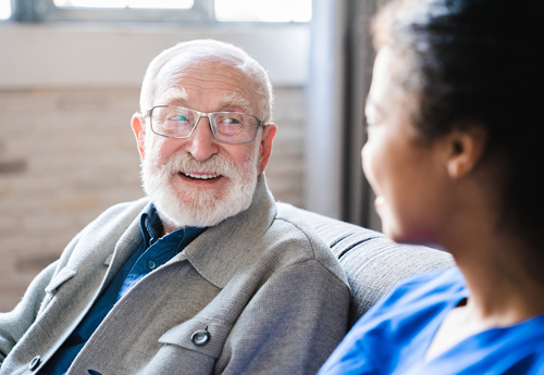 smiling elderly man talking with caregiver in a comfortable setting discussing care options to improve quality of life and well being